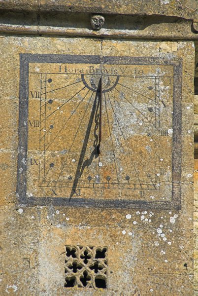 Sundial on the south wall of the church. The Latin inscription translates very roughly as 'Time is Short'. Photo of St Andrew's Church, Chedworth, Gloucestershire.