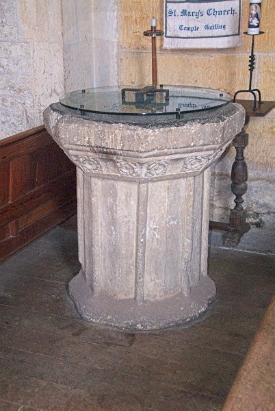 The simply decorated and somewhat battered 15th century font. Photo of St Mary's Church, Temple Guiting, in the Gloucestershire Cotswolds. Part of the Britain Express Travel and Heritage Picture Library.