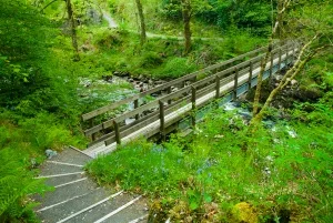 The path drops down to a narrow footbridge across the River Kinglas