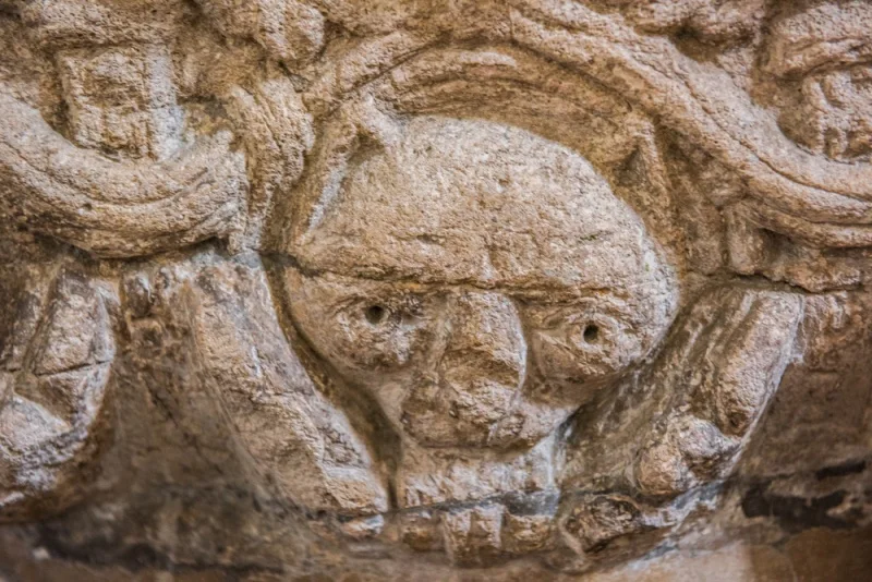Carved figure of a grinning cat on the font
