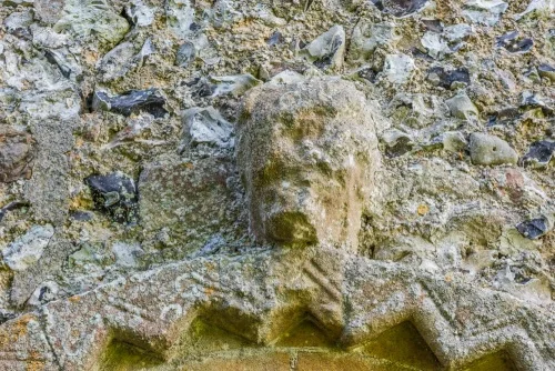 A weathered carved head over the north door