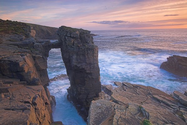 Dramatic photo of a natural arch with the sea foaming around its base. Photo taken at Yesnaby, Orkney Mainland, Scotland.