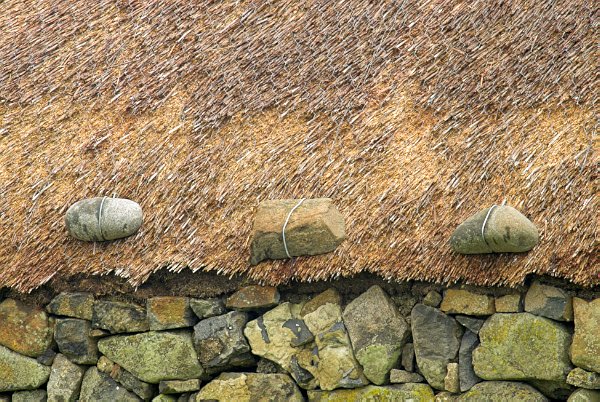 Thatched roof at Kilmuir. Traditionally these roofs are netted and anchored with heavy weights, like these stones, to stop them from being damaged in high winds. Stock photo of Kilmuir on the Isle of Skye, Scotland. Part of the Britain Express Travel and Heritage Picture Library, Scotland collection.