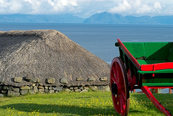 Photo of a colourfully painted farm cart and a thatched building at the Skye Museum of Island Life at Kilmuir. Part of the Britain Express Travel Guide to the Isle of Skye.