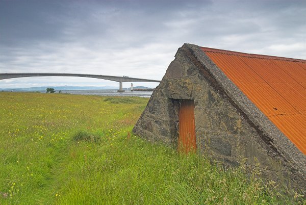 This small hut sunk into green grass makes a large statement with it's orange roof and door. The Skye Bridge appears in the background. Stock photo of the Skye Bridge on the Isle of Skye, Scotland. Part of the Britain Express Travel and Heritage Picture Library, Scotland collection.