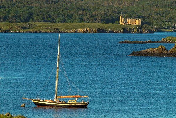 A boat bobs at anchor in Loch Dunvegan, with Dunvegan Castle on the far shore. Stock photo of Dunvegan Castle on the Isle of Skye, Scotland. Part of the Britain Express Travel and Heritage Picture Library, Scotland collection.