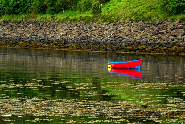A colourful boat is reflected in the harbour at Portree. Stock photo of Portree on the Isle of Skye, Scotland. Part of the Britain Express Travel and Heritage Picture Library, Scotland collection.