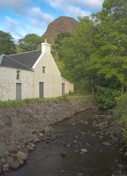 This whitewashed cottage has a high rocky hill looming behind it. Stock photo of Talisker on the Isle of Skye, Scotland. Part of the Britain Express Travel and Heritage Picture Library, Scotland collection.