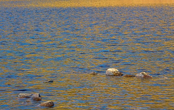 The sun rises over an inland loch near Staffin. The mustard yellow of the hills is dappled through the blue water. Stock photo of Staffin on the Isle of Skye, Scotland. Part of the Britain Express Travel and Heritage Picture Library, Scotland collection.