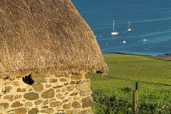A thatched cottage with a sea view. Note the stones hanging from the thatch. These are attached to nets and are necessary to prevent the thatch from being blown off. Stock photo of the coast at Stein on the Isle of Skye, Scotland. Part of the Britain Express Travel and Heritage Picture Library, Scotland collection.